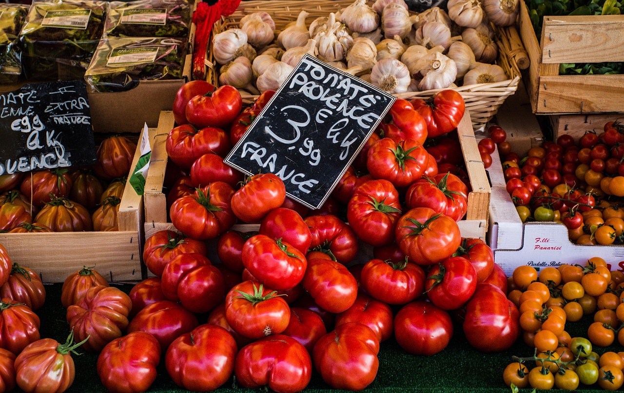 Crates of ripe red peppers, tomatoes and garlic at a market with a chalkboard price sign, representing food safety