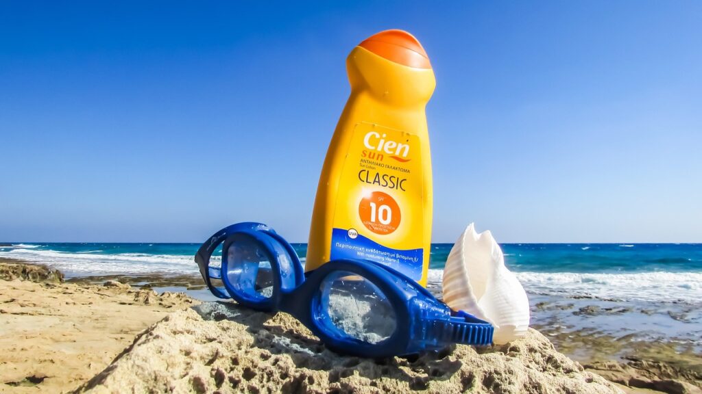 Yellow sun lotion bottle with swim goggles and a seashell on a beach, representing octocrylene in sunscreen
