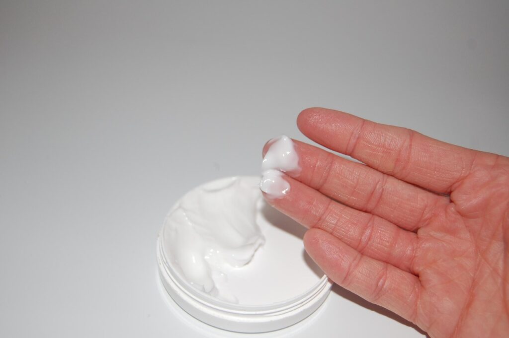 Hand scooping white moisturizing cream from a small tub, representing parabens in cosmetics and creams