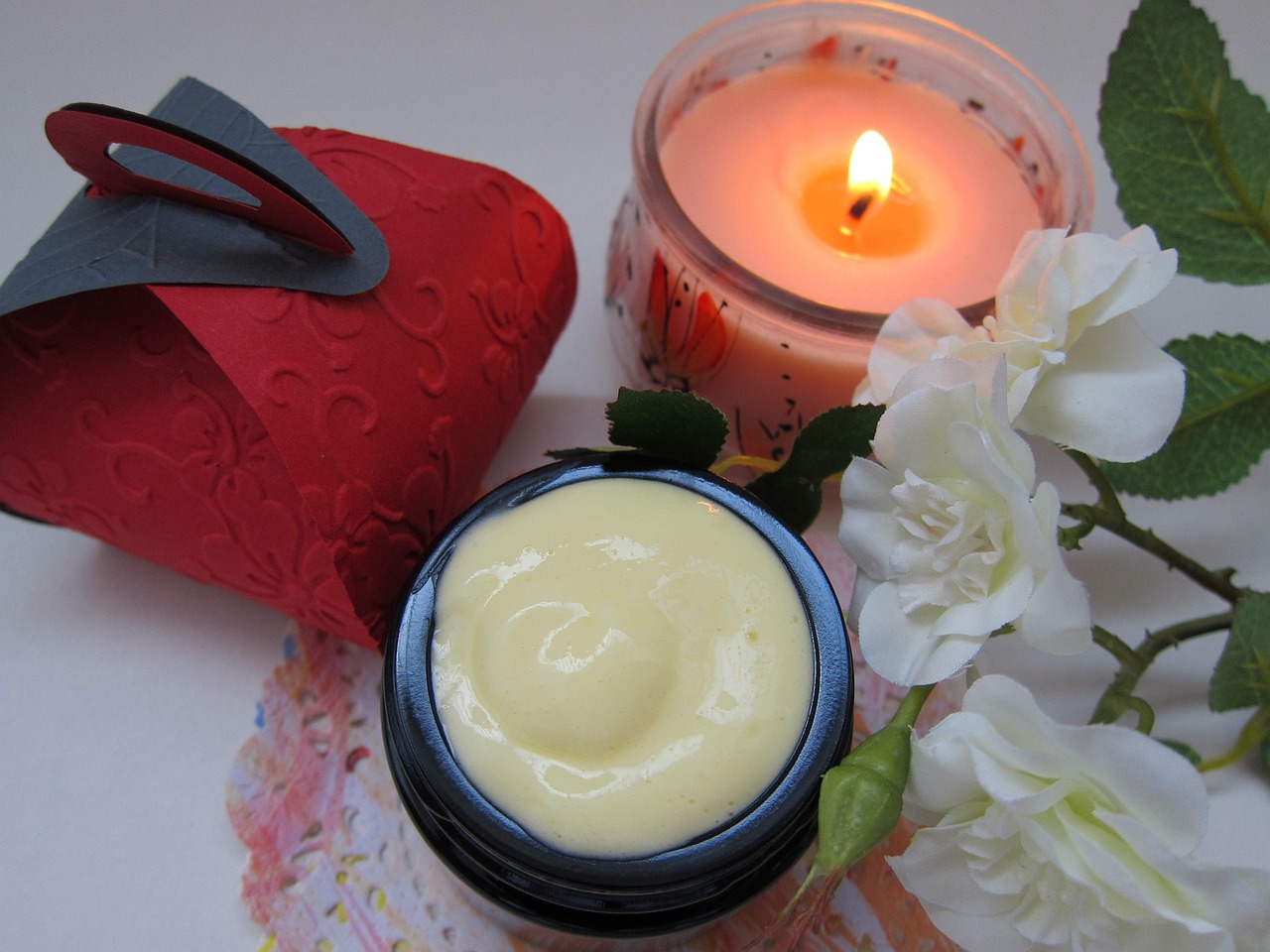 Jar of creamy moisturizer beside white flowers and a candle, representing skincare brand choices during pregnancy