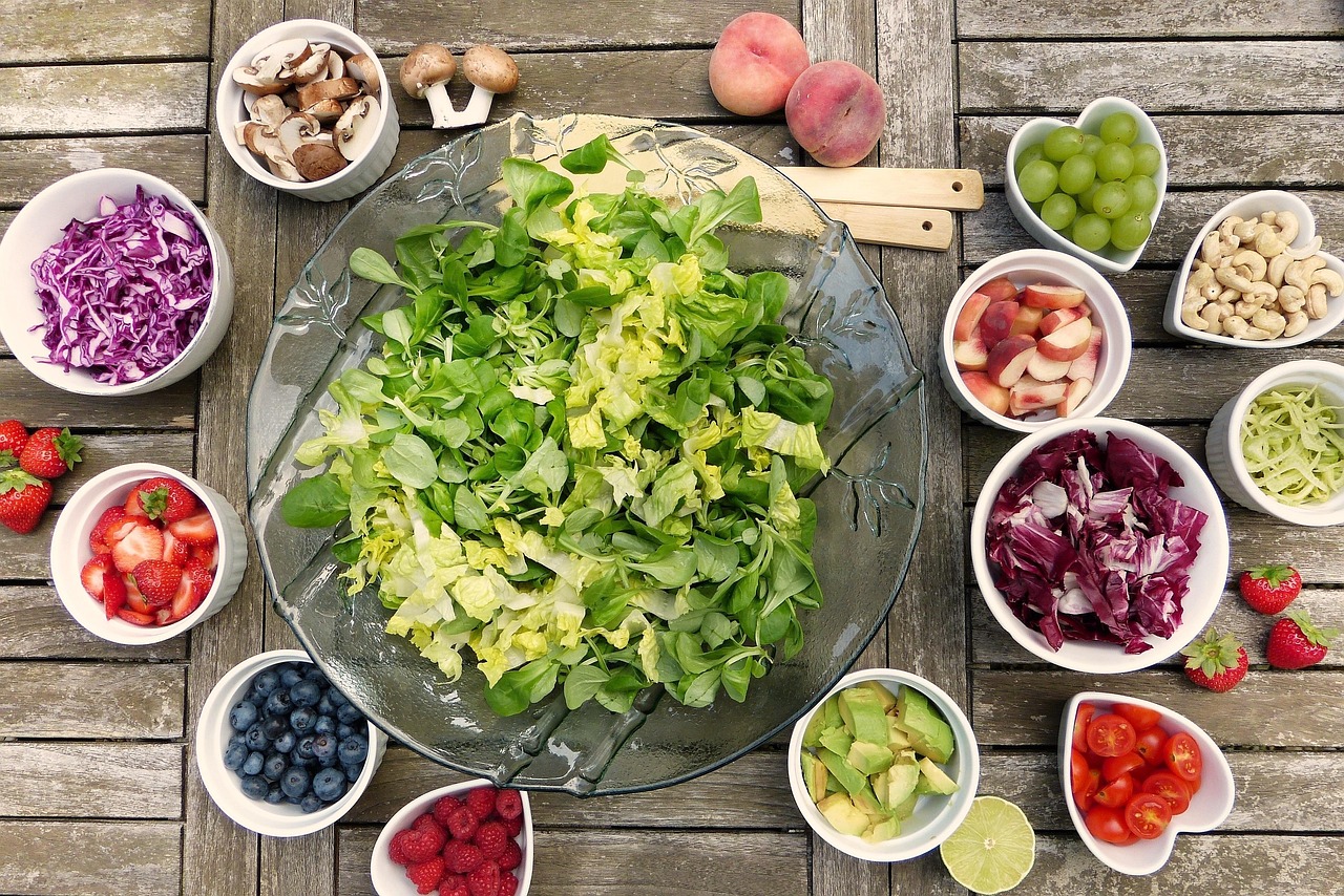 Overhead view of a glass bowl of fresh salad greens surrounded by bowls of berries, nuts and vegetables, representing pregnancy food choices