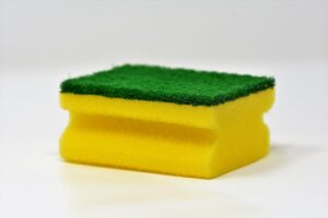 Yellow and green cleaning sponge on a white surface, representing what to use and avoid when cleaning in pregnancy
