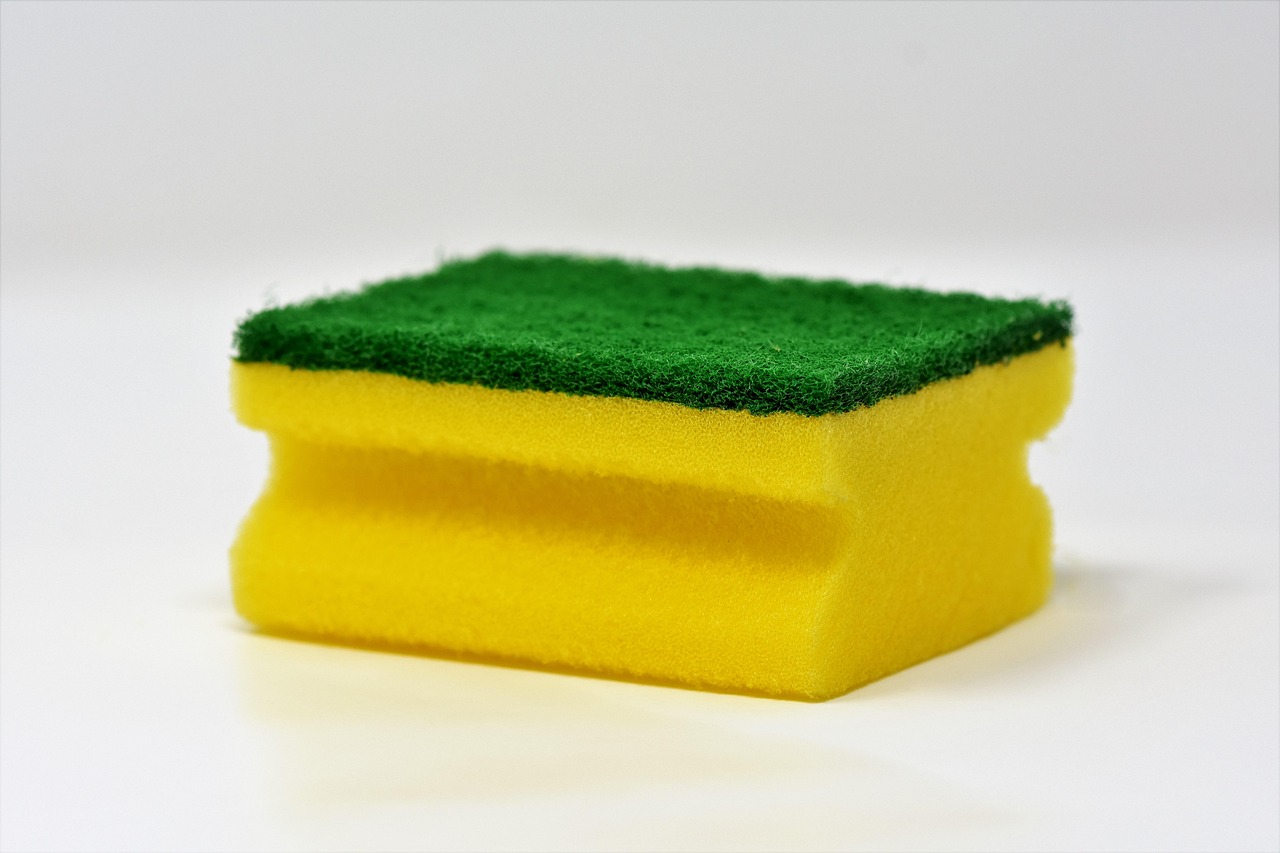 Yellow and green cleaning sponge on a white surface, representing what to use and avoid when cleaning in pregnancy