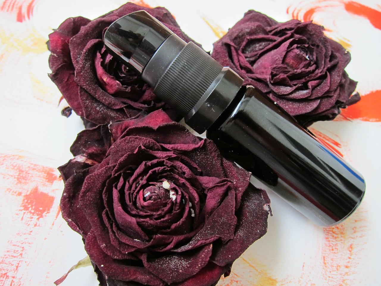 Black pump serum bottle resting on dark red dried roses, representing gentle cosmetics for sensitive skin in pregnancy