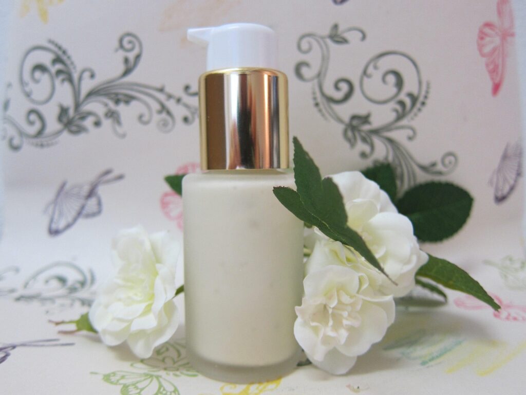 White pump bottle of body lotion with a gold cap beside white flowers and green leaves, representing pregnancy-safe body care