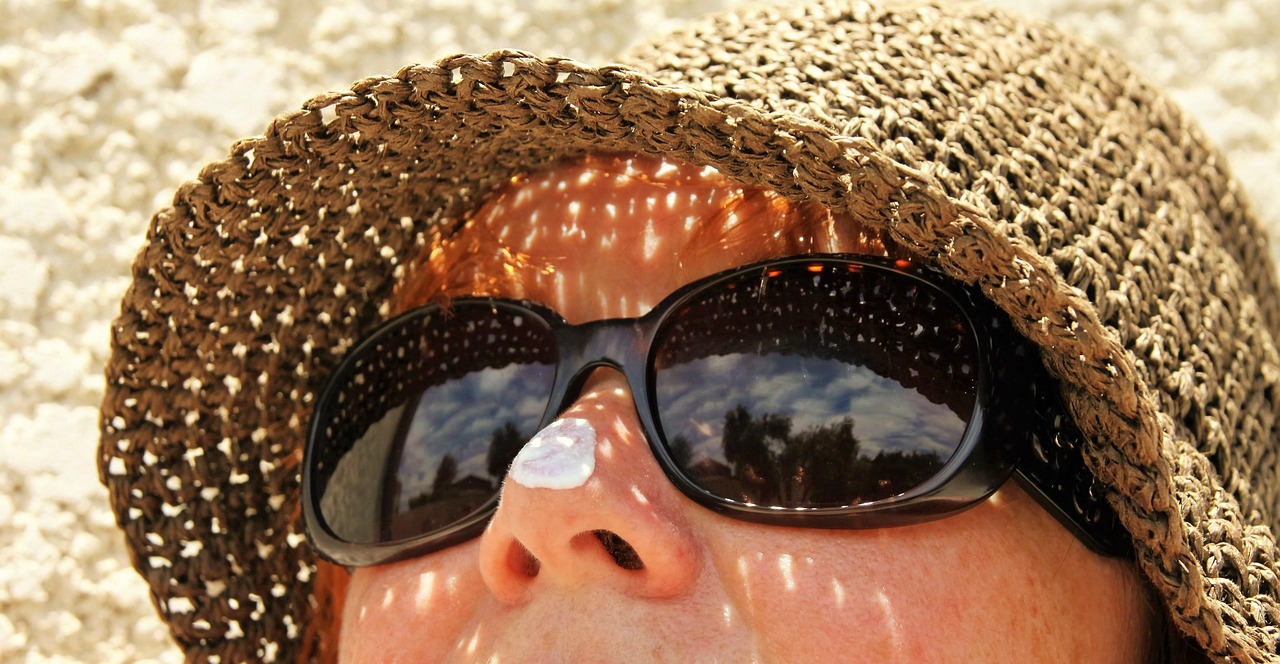Woman in a straw hat and sunglasses with a dab of sunscreen on her nose, representing sunscreen safety in pregnancy