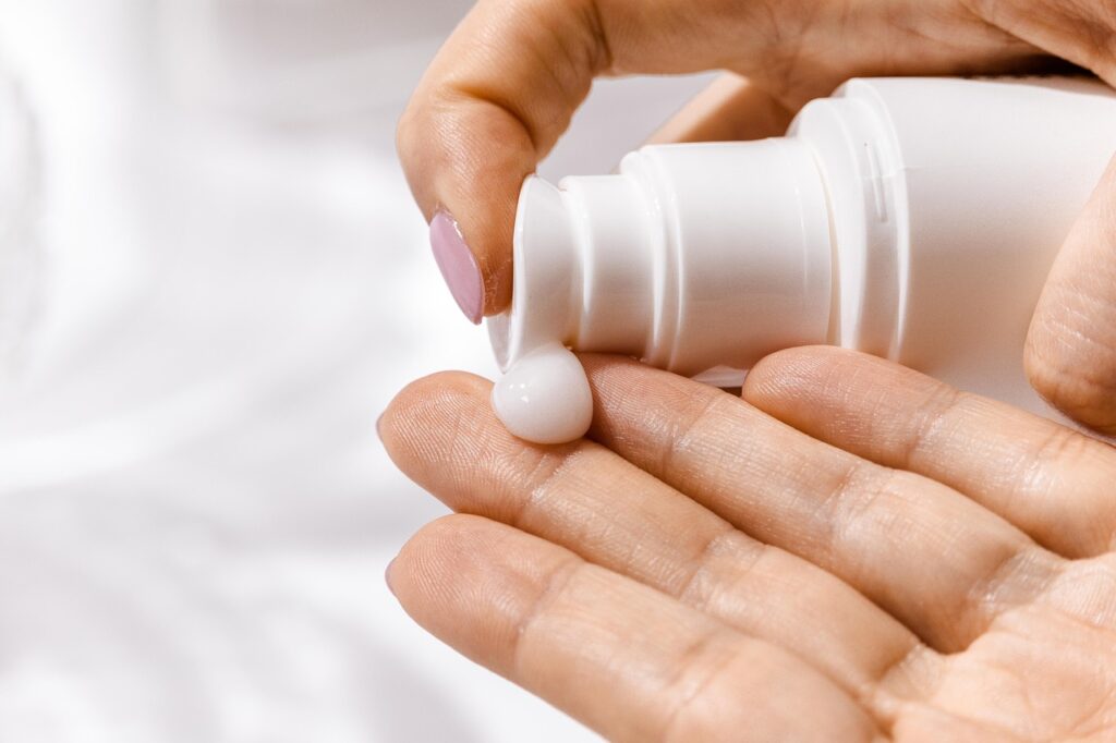 Hand squeezing white lotion from a pump bottle onto fingertips, representing mineral sunscreen application