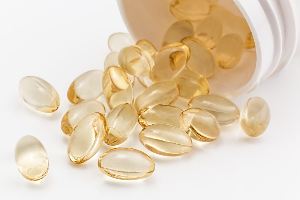 Clear softgel vitamin capsules spilling from a white bottle, representing prenatal vitamins
