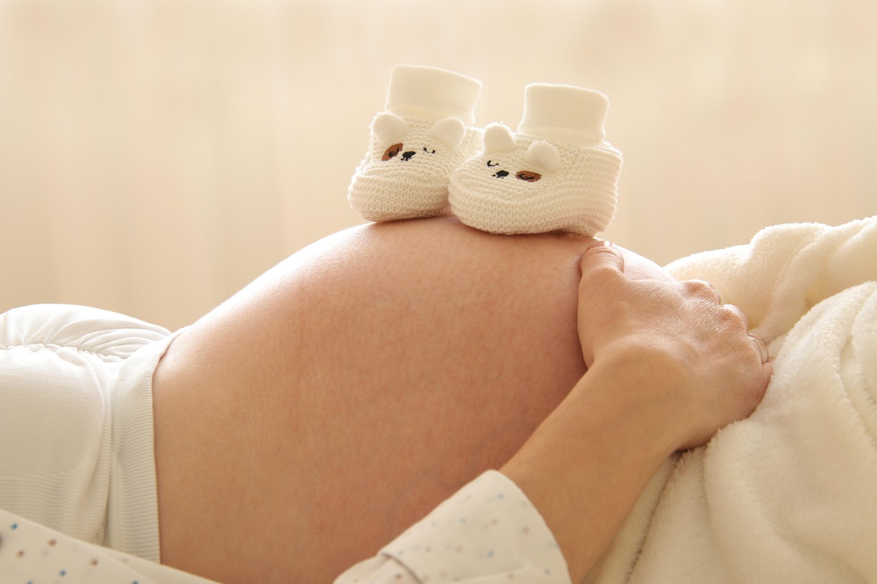 Small white baby booties resting on a pregnant belly, representing preparing for a new baby