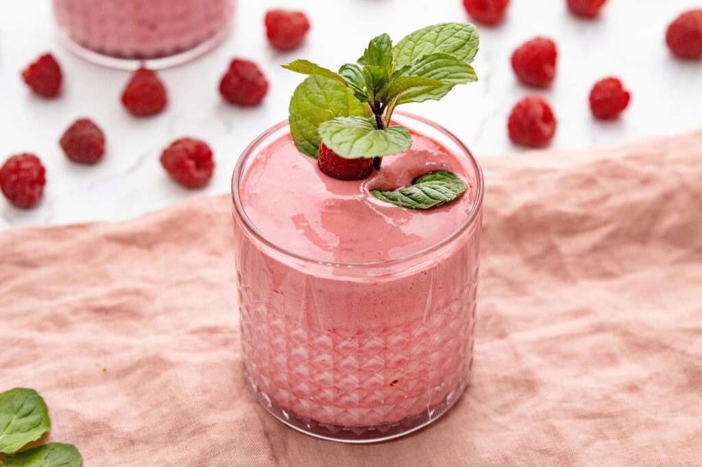 Pink berry smoothie in a glass topped with raspberries and mint, representing a protein shake during pregnancy