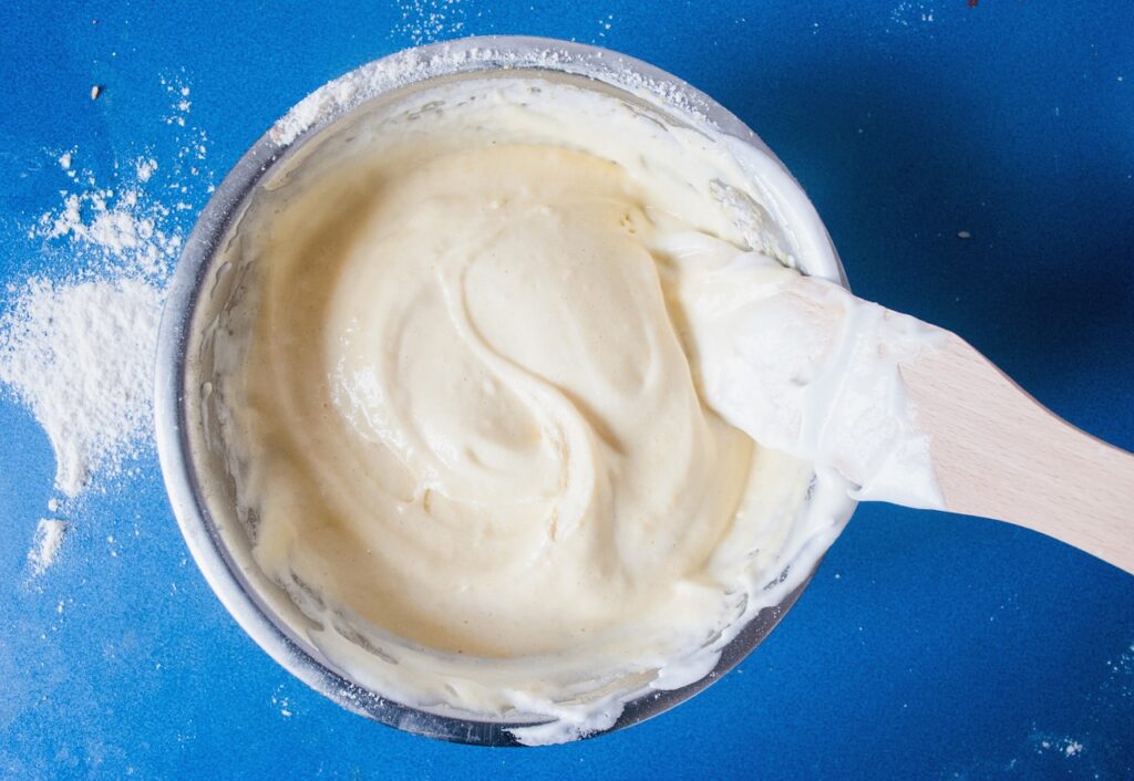 Bowl of raw cookie dough batter with a spatula on a blue surface, for the raw dough pregnancy question