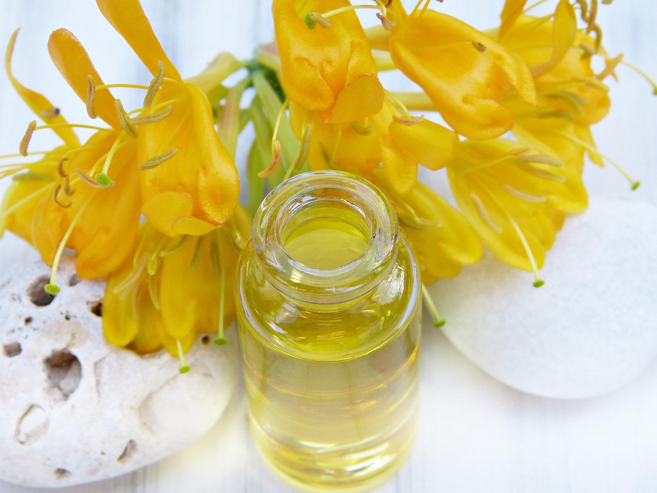 Clear glass bottle of golden oil beside yellow flowers, representing retinol alternatives and serum skincare in pregnancy