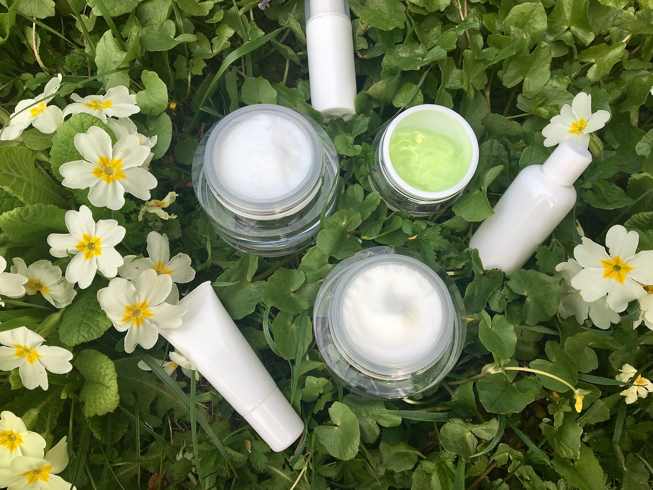 Jars and tubes of white cream among small white flowers on grass, representing retinol creams and serums compared