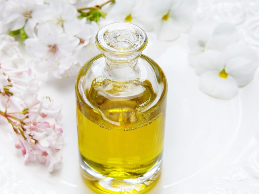 Glass bottle of golden facial oil surrounded by white blossoms, representing rosehip oil skincare
