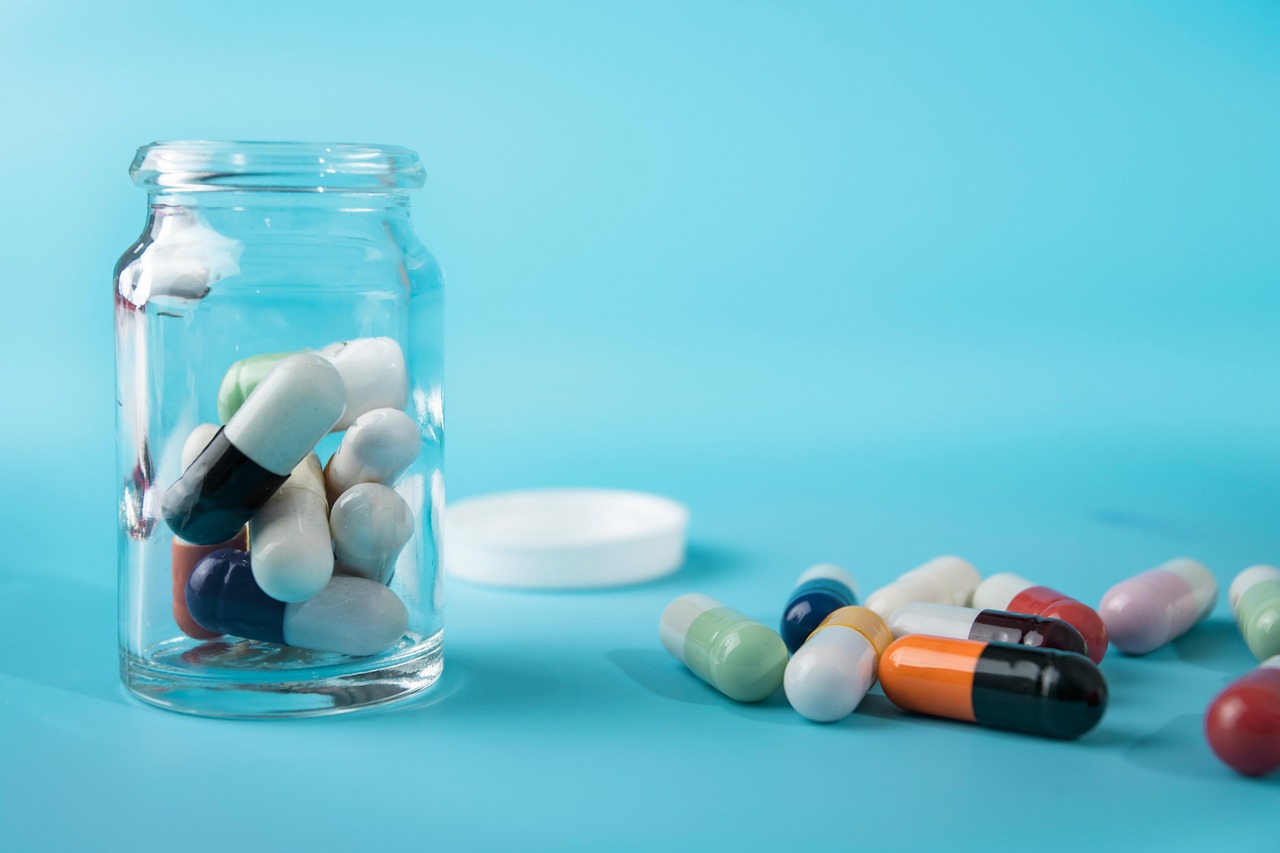 Glass bottle of capsules beside scattered colorful capsules on a blue surface, representing cold medicine