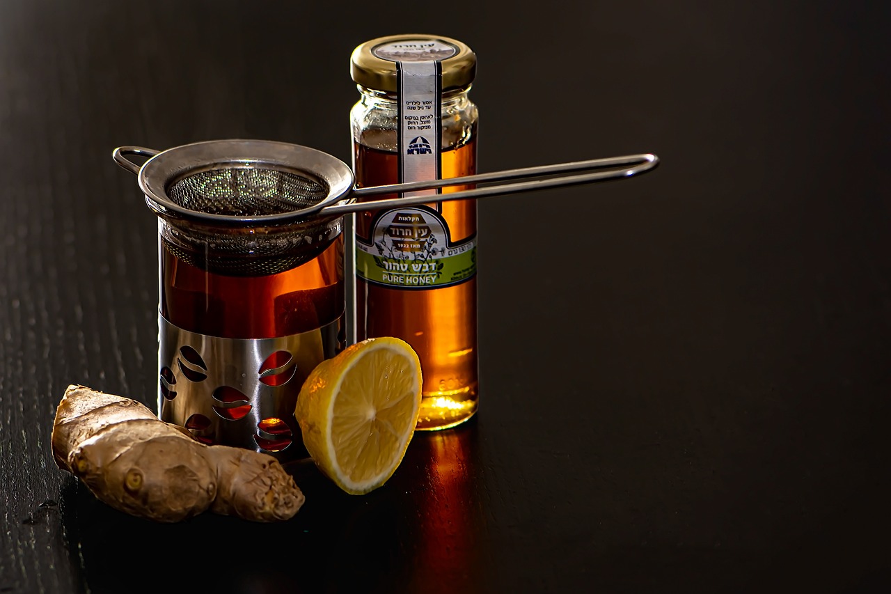 Cup of ginger and lemon tea beside honey and fresh ginger root, representing cold remedies