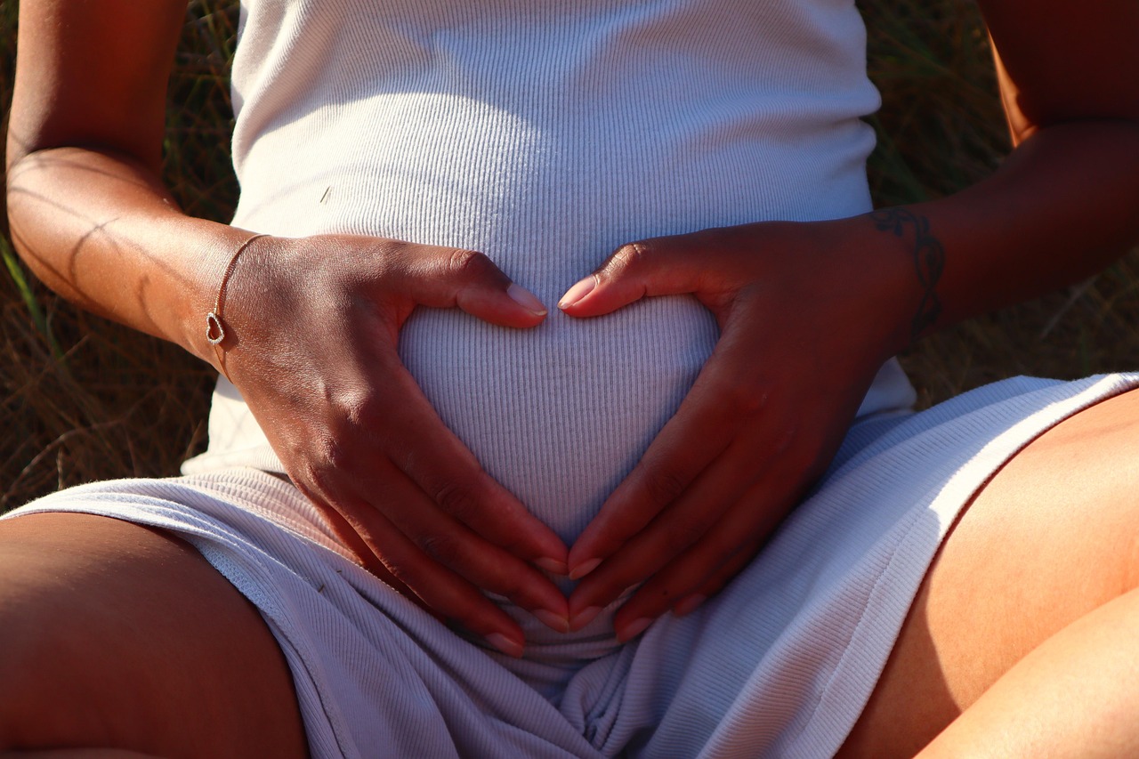 Pregnant woman with heart hands on her belly, anticipating motherhood with a SafeMom free trial for no surprises.