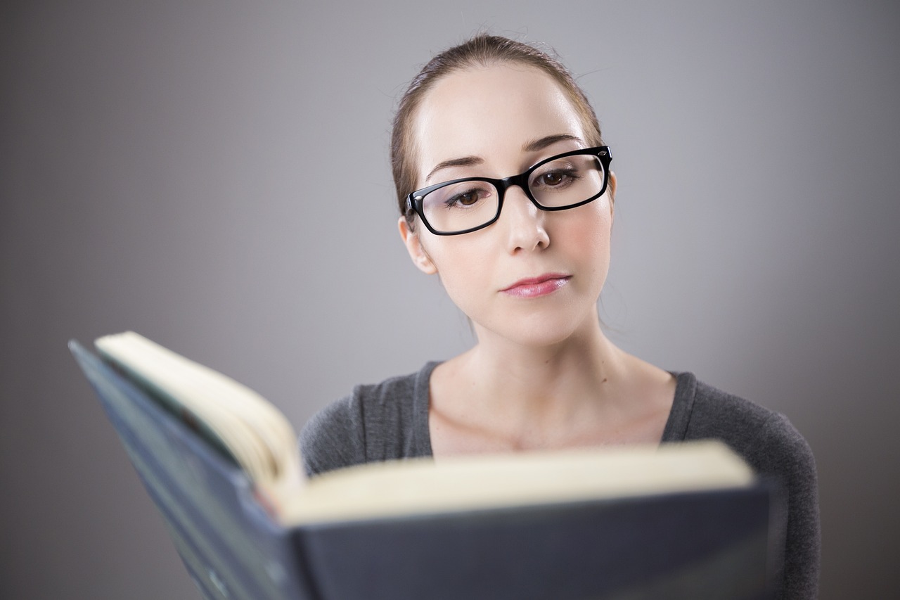 Woman in reading glasses meticulously studying a book, reflecting the diligence needed for SafeMom ingredient accuracy.