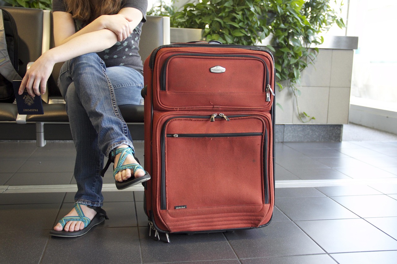 Red suitcase standing beside a traveler seated in an airport waiting area, representing travel-ready pregnancy-safe planning