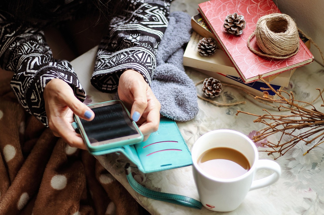 Hands holding a smartphone beside a cup of coffee and books, representing scanning products with the SafeMom app