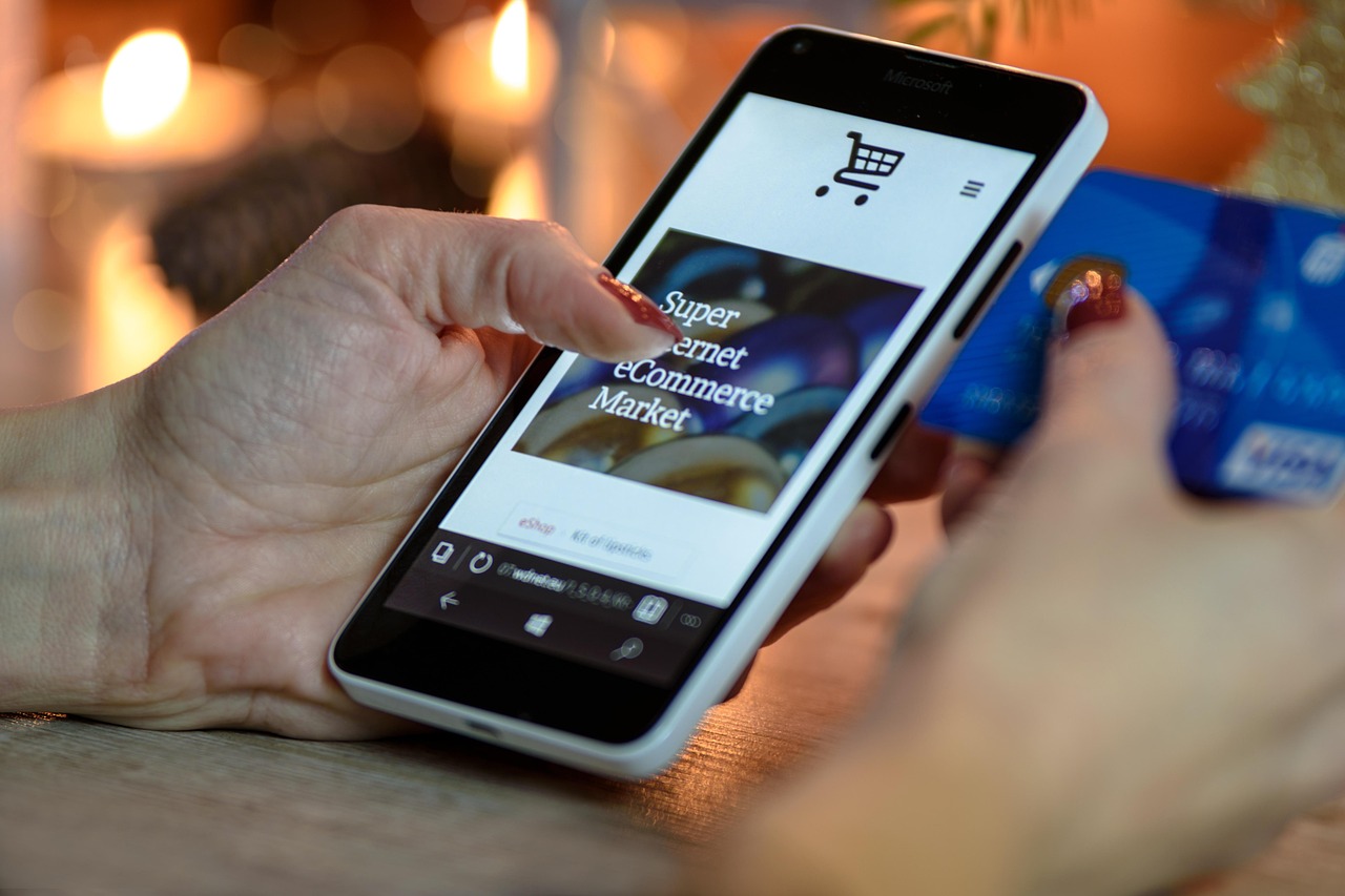 Hand holding a smartphone with an online shopping page beside a credit card, representing app subscription billing