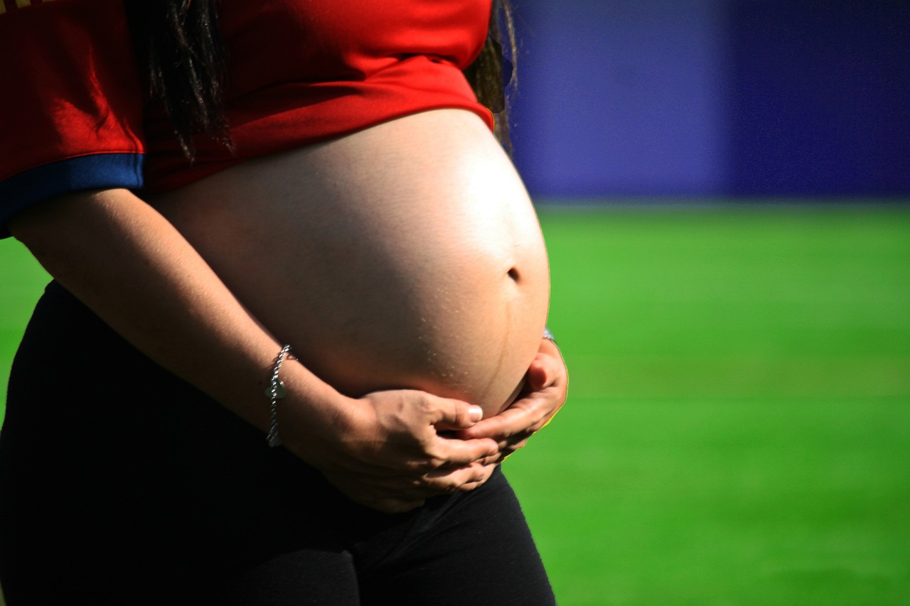 Pregnant woman cradling her bare belly on a sunlit field, representing the pregnancy ingredient safety index