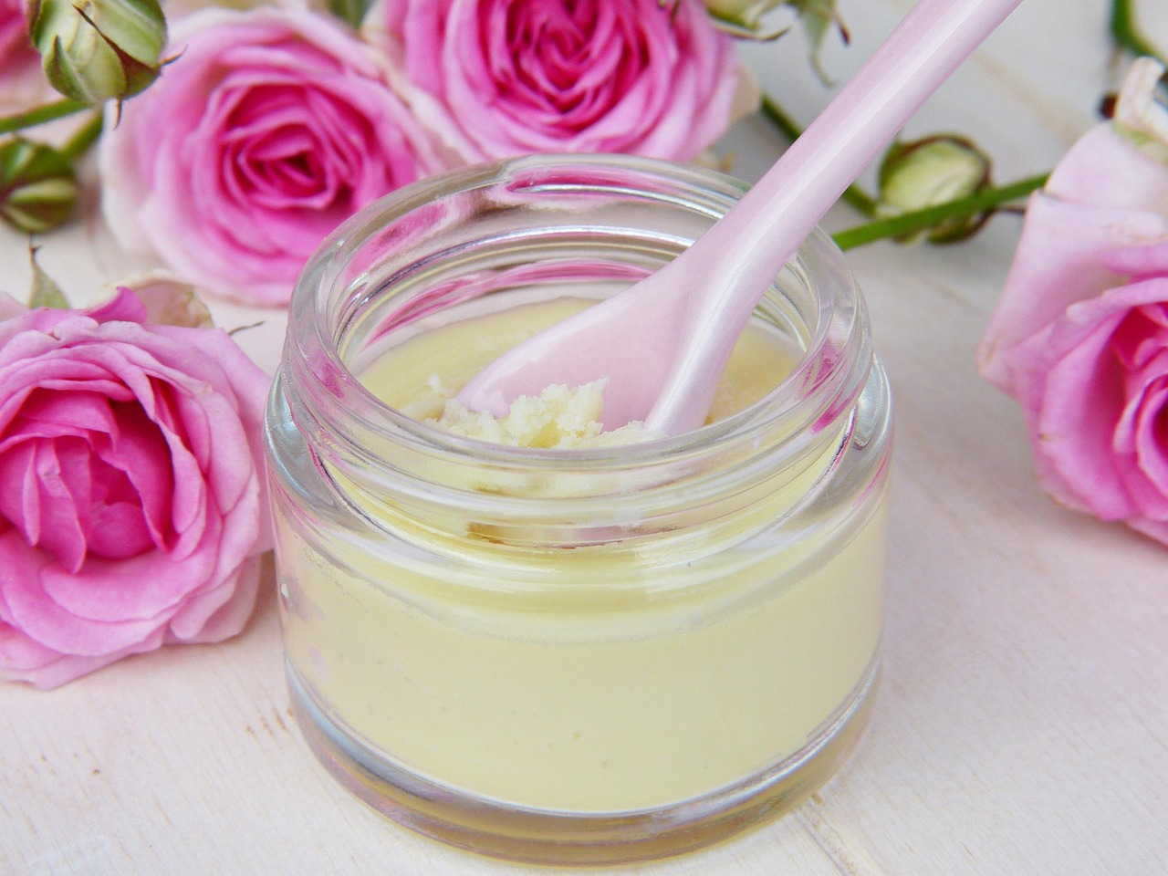 Glass jar of cream with a pink spoon among roses, representing gentle skincare choices in pregnancy