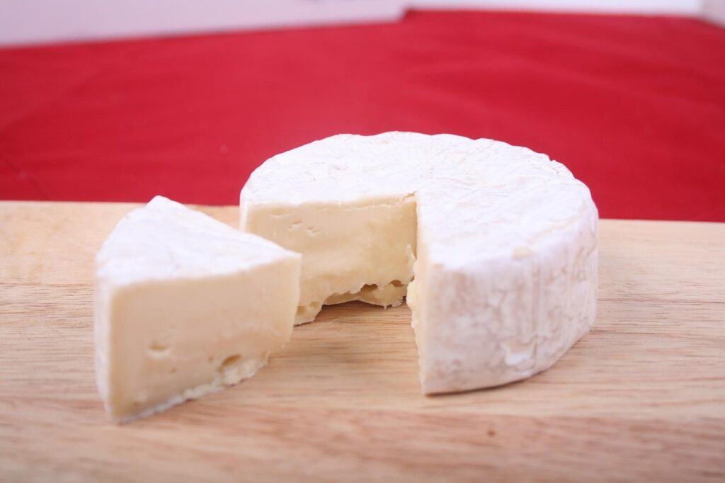 Whole white-rind brie cheese wheel with a wedge cut out on a wooden board, relevant to soft cheese in pregnancy