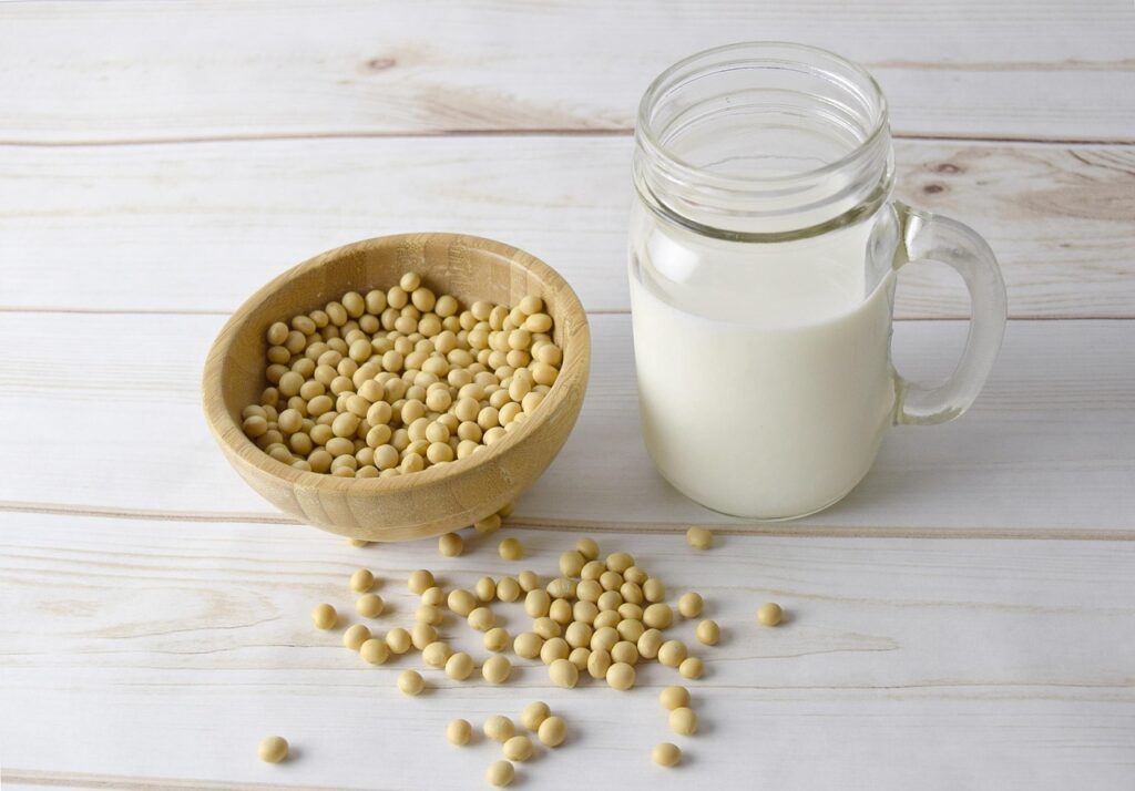Wooden bowl of soybeans beside a glass jar of soy milk on a white table