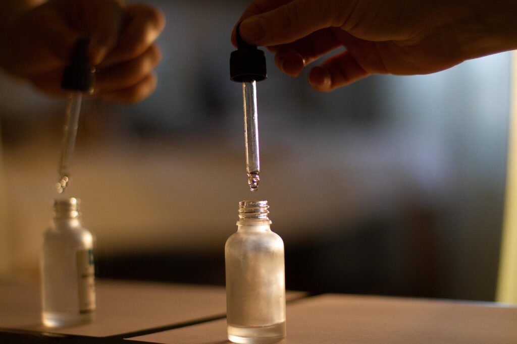 Hands holding glass dropper over small bottles of facial oil, representing squalane skincare oil