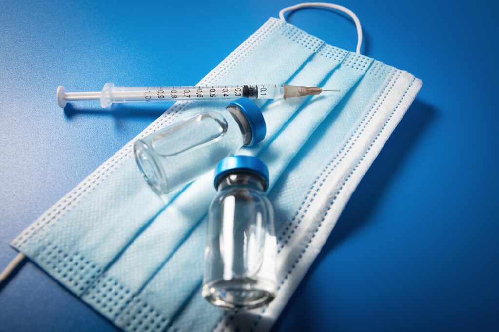 Syringe and glass vial resting on a blue surgical mask, illustrating the Tdap vaccine question in pregnancy