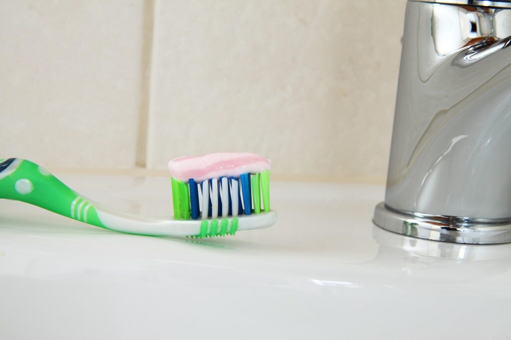 Green toothbrush with toothpaste beside a bathroom sink faucet, representing tooth care and teeth whitening