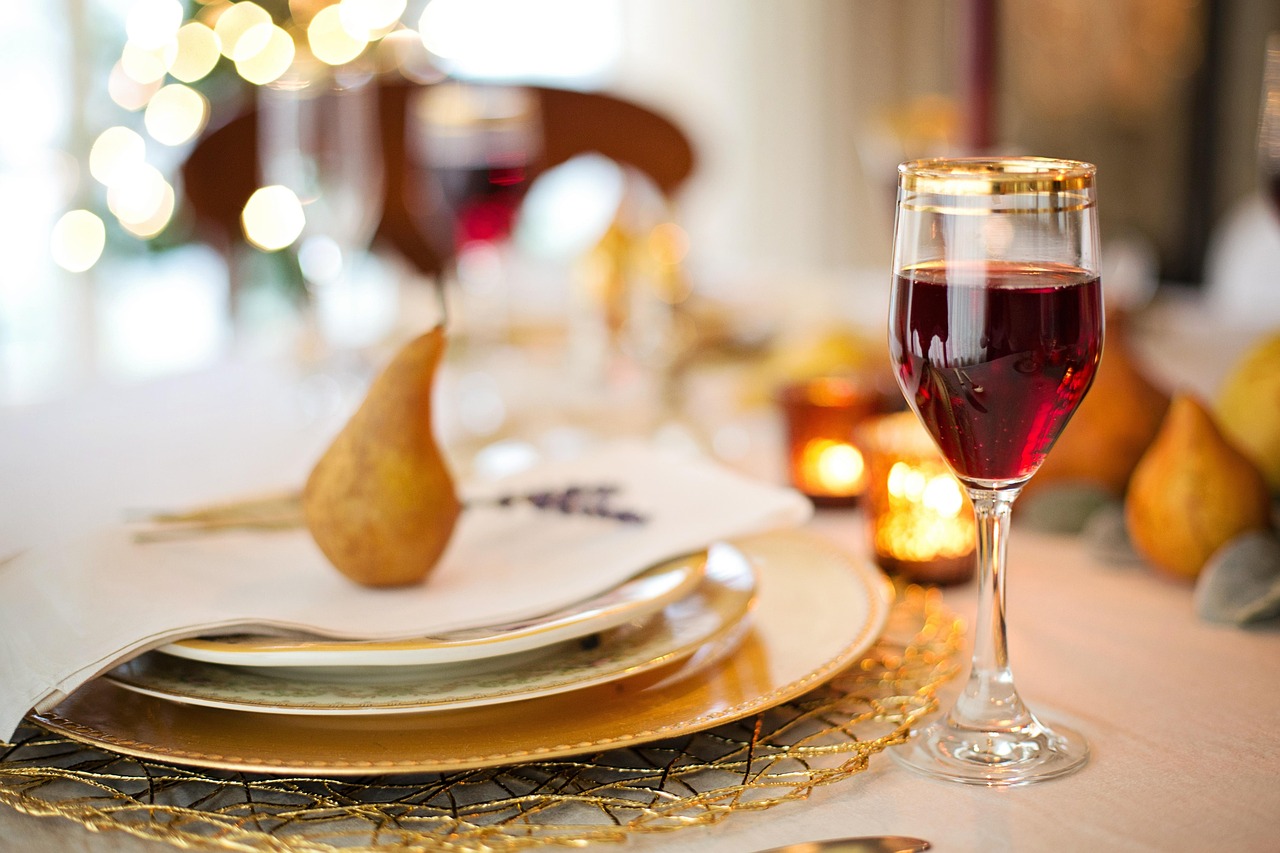 Thanksgiving table setting with a gold charger plate, pear, candles and a glass of red wine