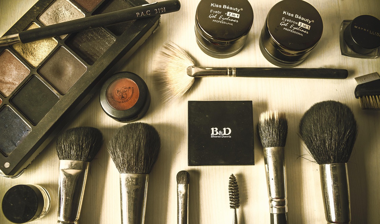 Makeup brushes and eyeshadow palette with cosmetic jars arranged on a table, representing ingredients in a makeup bag