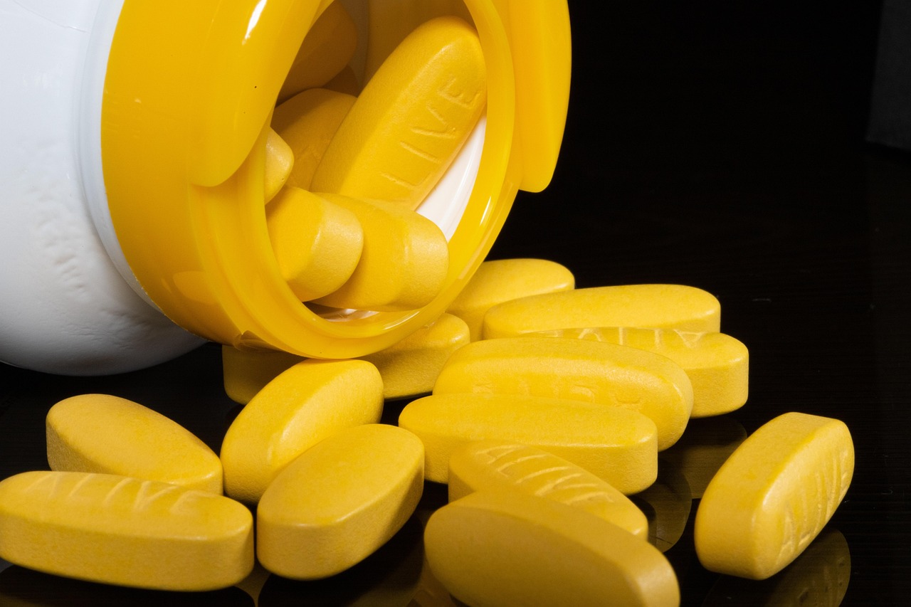 Yellow supplement tablets spilling from a white bottle on a dark surface, representing iron supplements in pregnancy