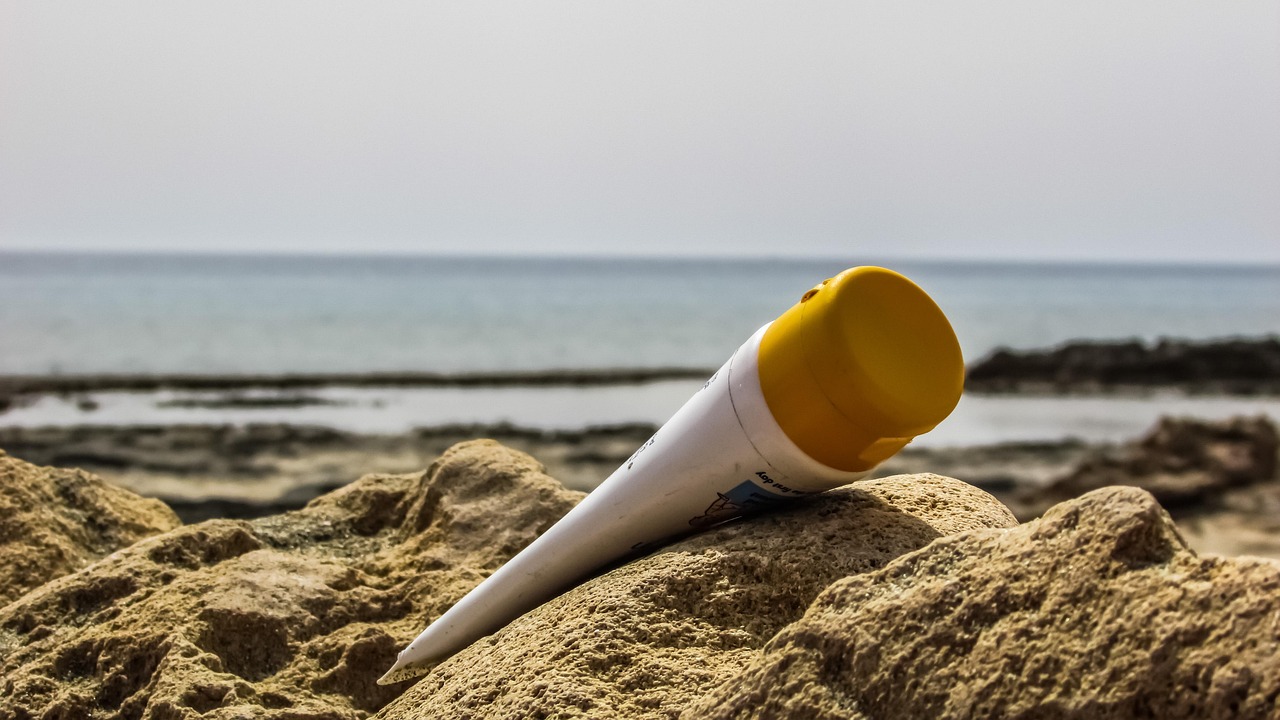 Sunscreen tube with a yellow cap resting on beach sand by the sea, representing safe sunscreen ingredients in pregnancy