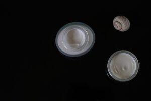 Two open jars of white face cream on a black surface, representing skincare for expecting moms