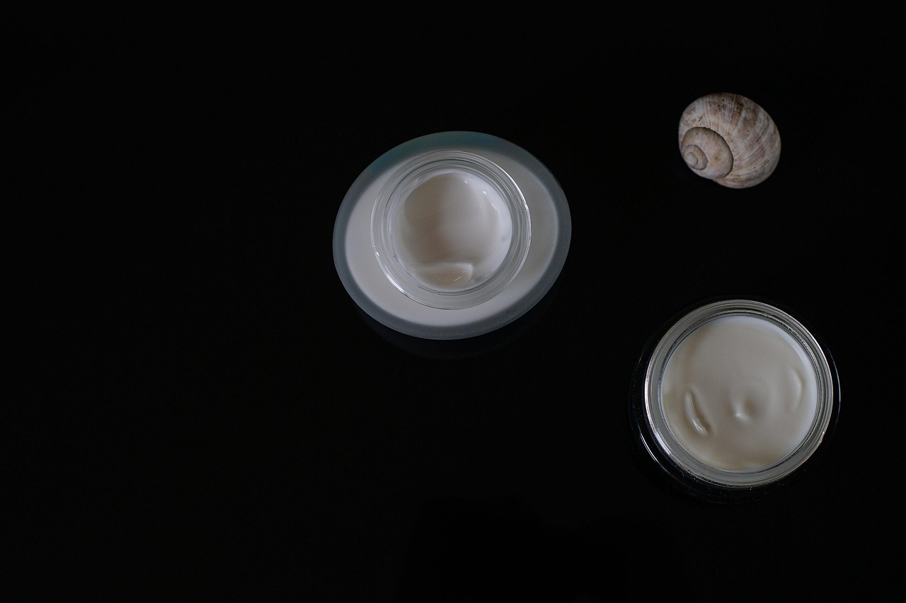 Two open jars of white face cream on a black surface, representing skincare for expecting moms