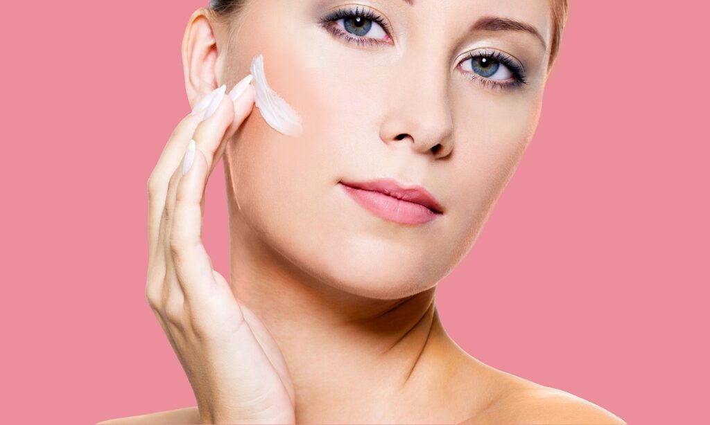 Woman with pink background smoothing a dab of cream onto her cheek, representing topical tretinoin cream and pregnancy