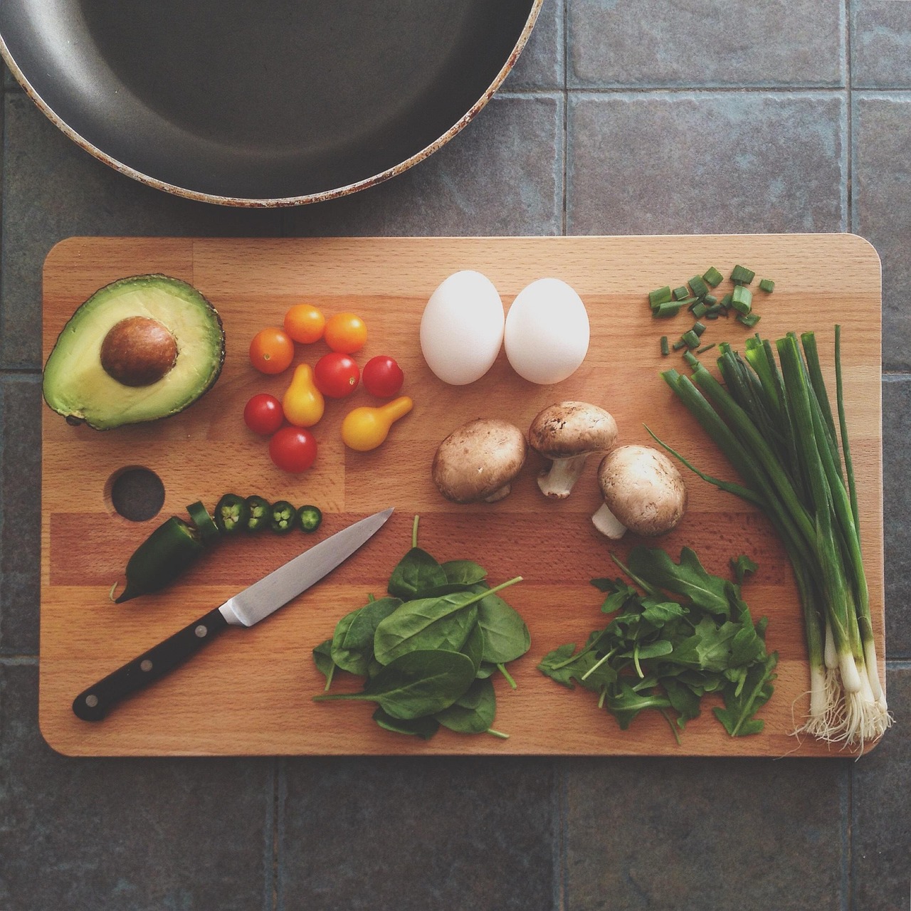 Avocado, eggs, mushrooms and fresh herbs on a wooden chopping board, representing food ingredients