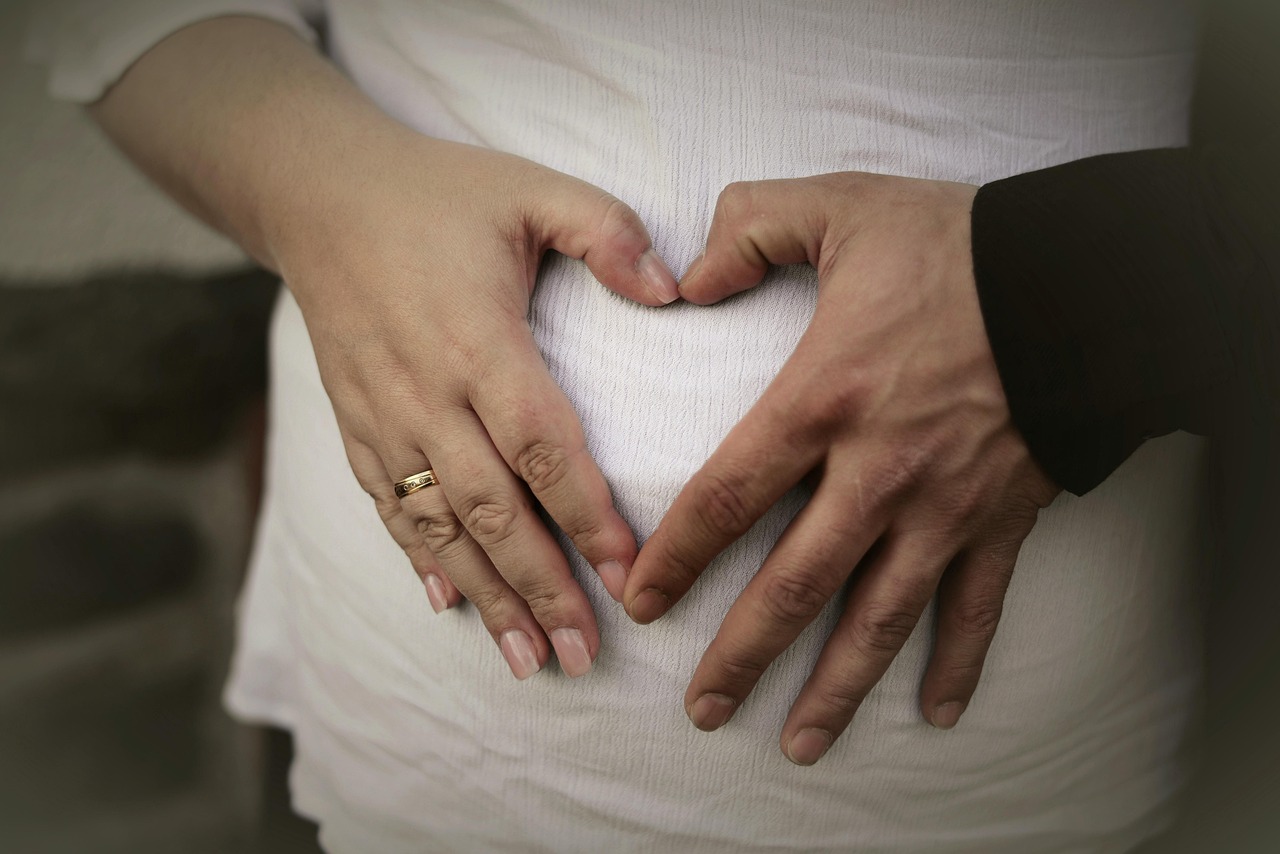 Couple's hands forming a heart over a pregnant belly in a white top, representing pregnancy and miscarriage risk by week
