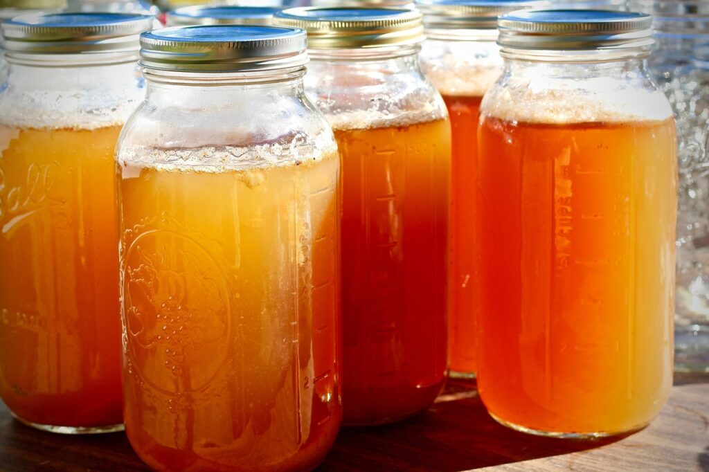 Glass jars of fresh amber apple cider in a row, illustrating unpasteurized juice and cider in pregnancy