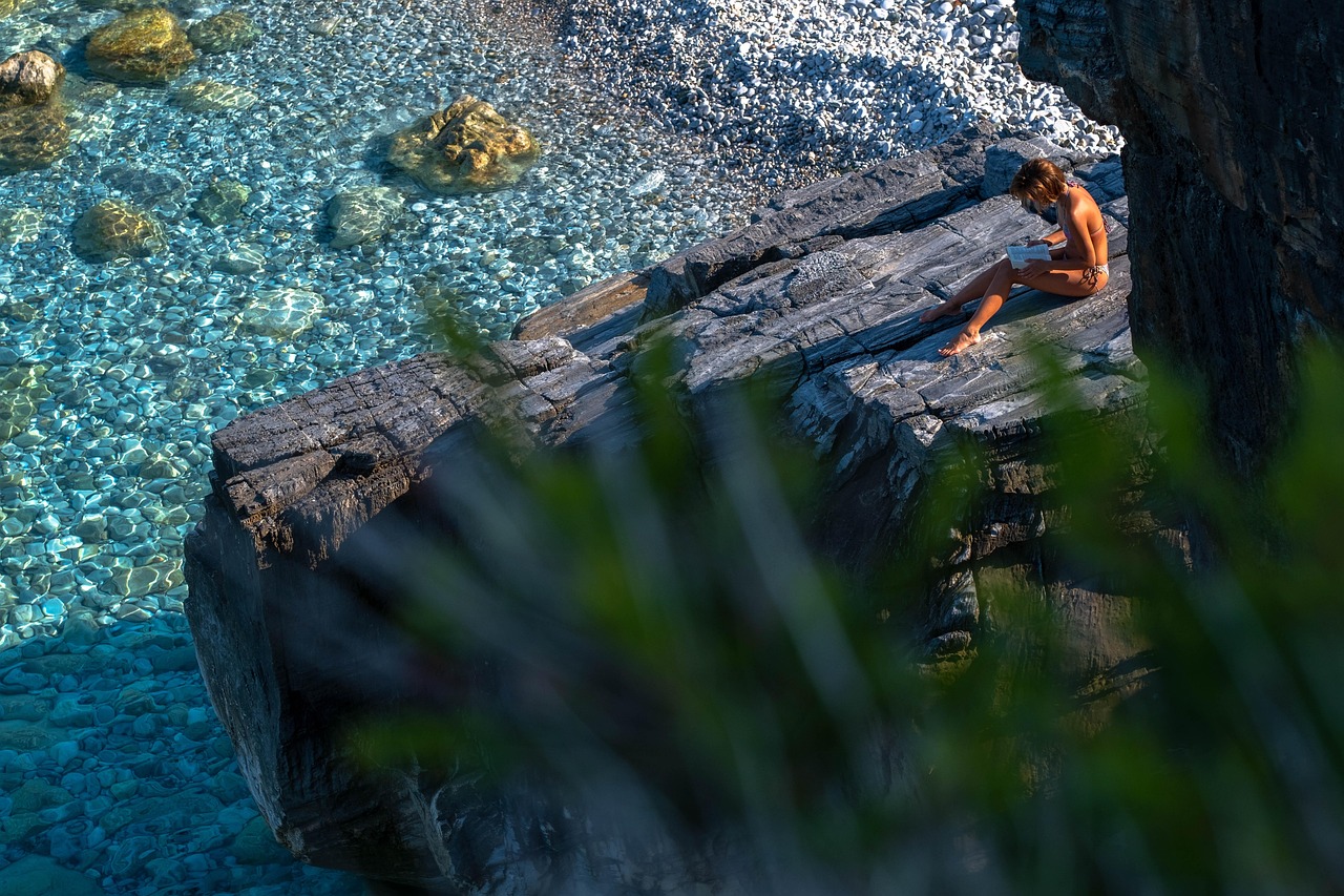 Woman reads a book on a rocky beach, comparing artificial sweeteners for pregnancy safety.