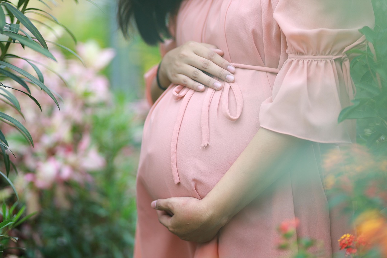 Smiling pregnant woman cradling her belly, beside fresh leafy greens, exploring their safety during pregnancy.