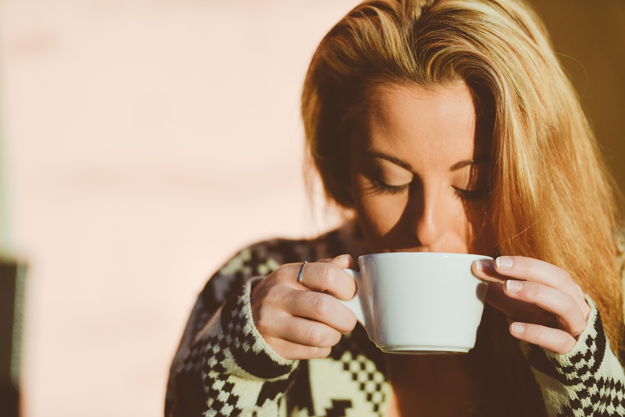 Blonde woman sips hot coffee from a mug, considering if Starbucks brewed coffee is safe during pregnancy.