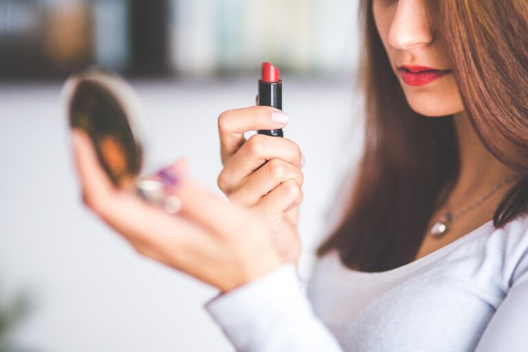Closeup of a woman applying red lip gloss in a mirror, considering if Neutrogena Hydro Boost Water Gel is safe during pregnan