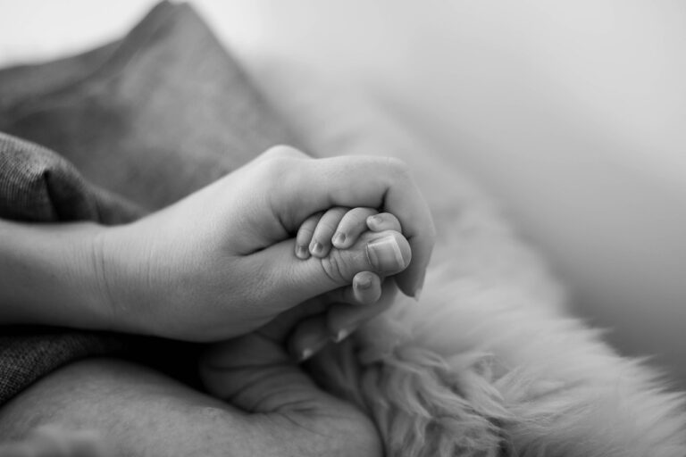 A black and white photo of a mother's hand holding a child's, highlighting COSRX Advanced Snail 96 Mucin Power Essence safety
