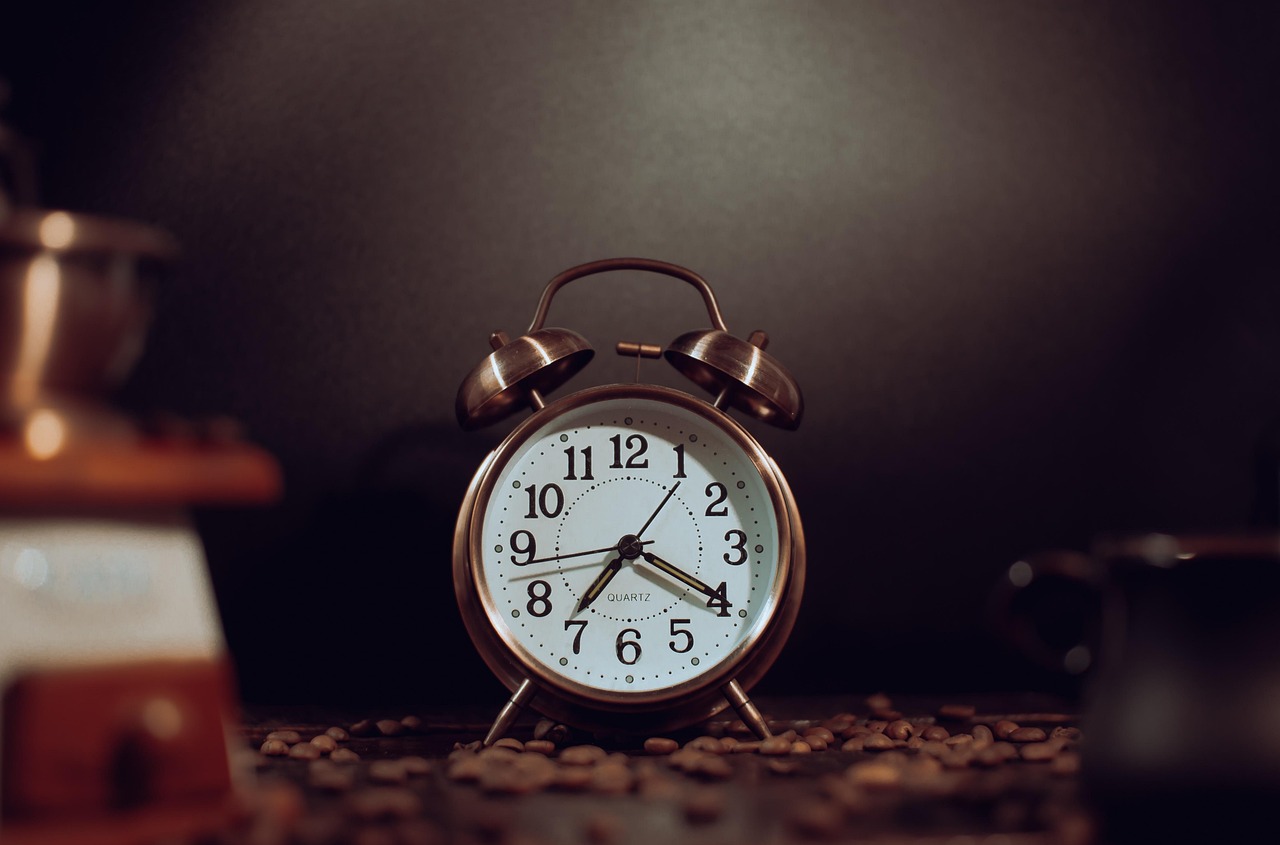 A coffee cup, grinder, and alarm clock on a table, raising questions about caffeine during pregnancy.